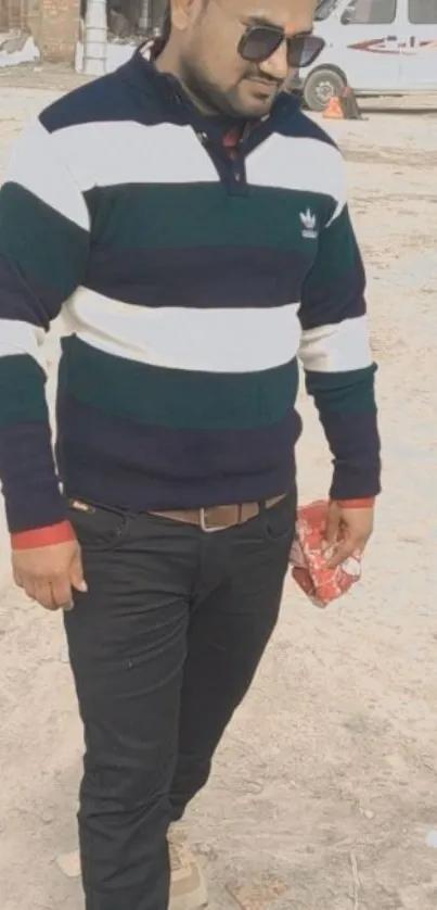 Man in striped sweater outdoors, holding bag.