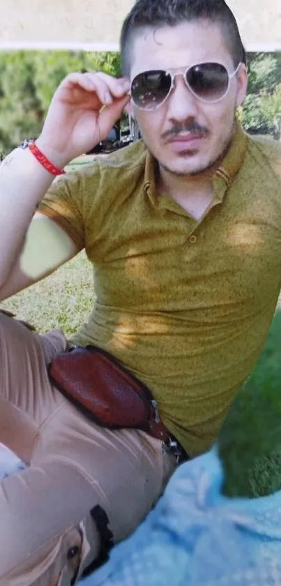 Casual style man in sunglasses outdoors with a green backdrop.