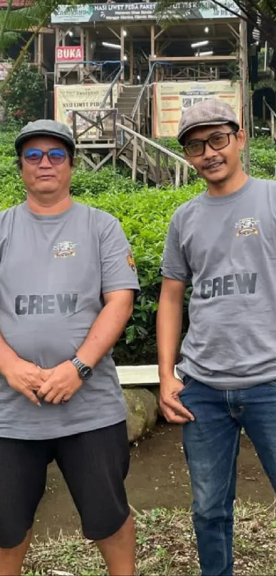 Two people in crew shirts outdoors with greenery.