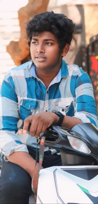 Young man in blue plaid shirt sitting on a scooter outdoors.