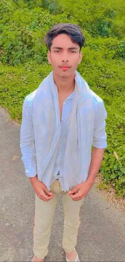 Young man in casual attire outdoors with green foliage background.