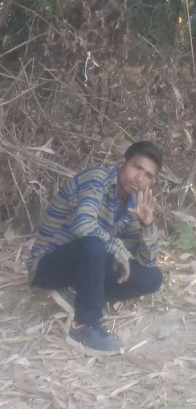 Man in striped shirt sitting outdoors against a bamboo backdrop.