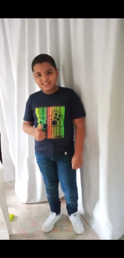 Young boy in a casual outfit with a graphic tee and jeans, standing indoors.