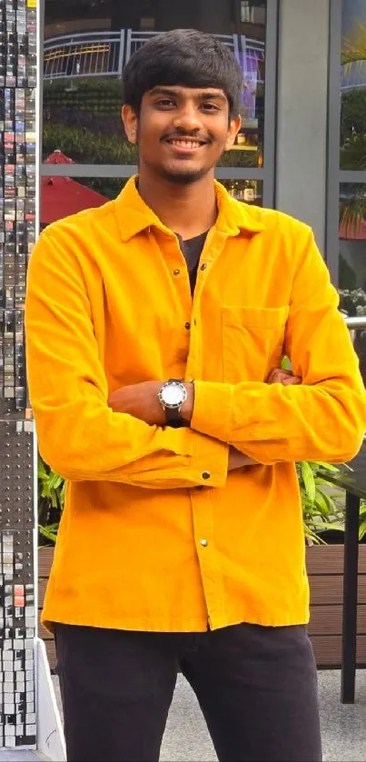 Young man in vibrant yellow shirt and black pants standing outdoors.