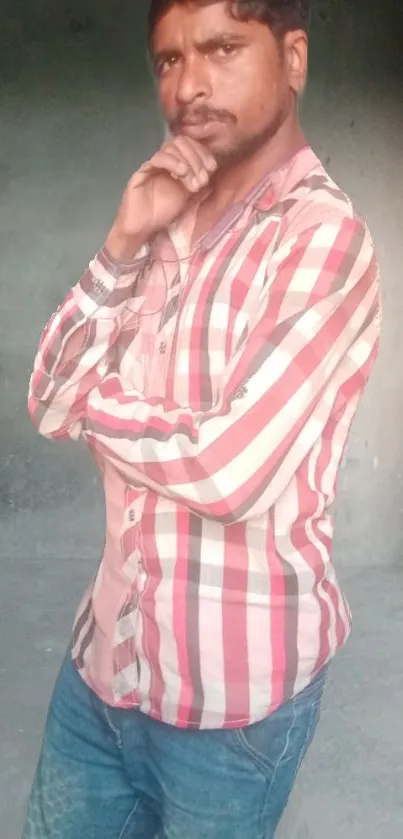 Man in plaid shirt striking a thoughtful pose in gray-walled room.