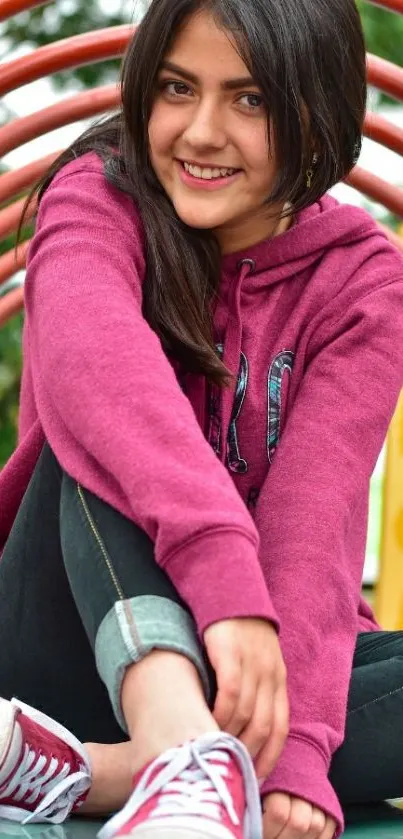 Young person in pink hoodie smiling seated in an artistic arch setting.