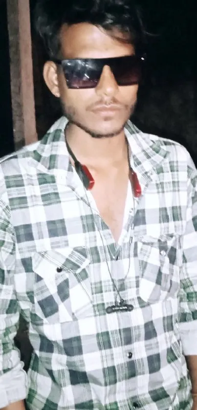 Young man in plaid shirt with sunglasses at night.