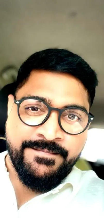 Casual portrait of a bearded man sitting inside a car, wearing glasses.