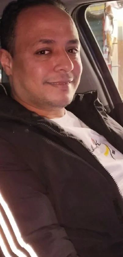 Man sitting inside a car at night, smiling casually.