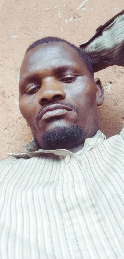 A person in a striped shirt resting against a rustic wall.