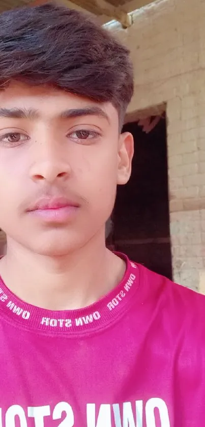 Portrait of a young man in a red shirt outdoors with a rustic background.