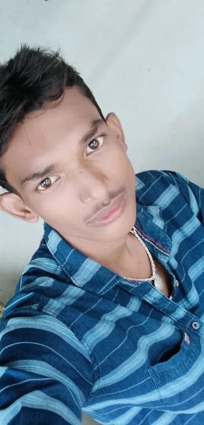 Portrait of a young man in a blue shirt with a neutral background.