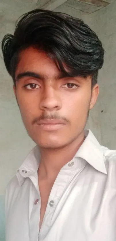 Portrait of a young man in a light shirt against a textured wall.