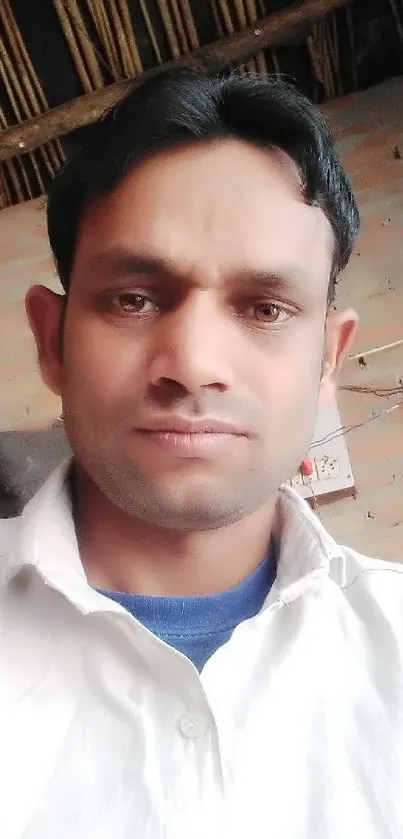 Man in a white shirt posing against a rustic background.