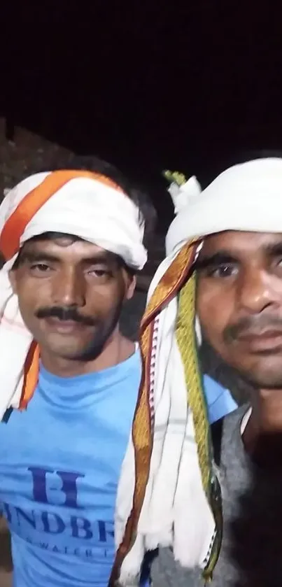 Two men with turbans in a casual portrait at night.