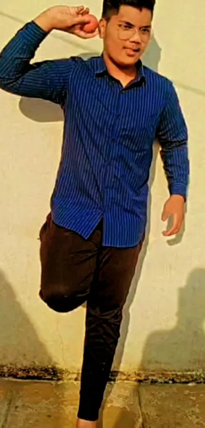 Casual pose of a young man against a sunlit beige wall.