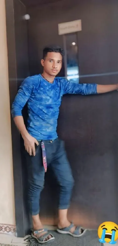 Young man in blue shirt posing casually against a wall.