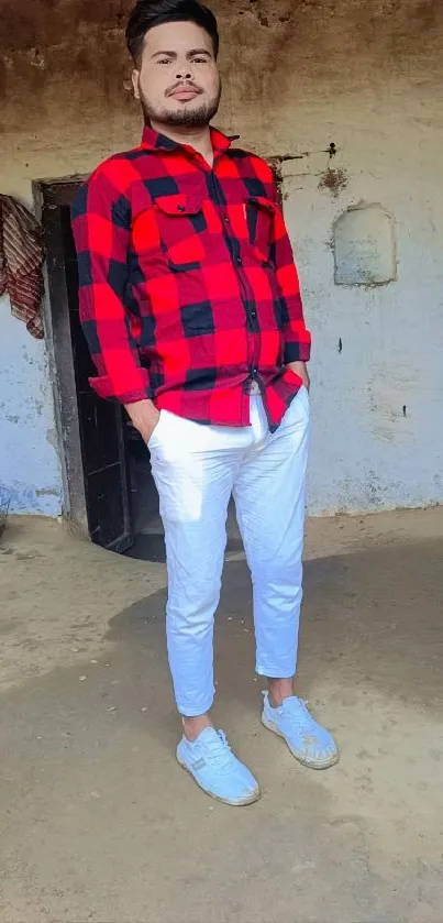 Person in red plaid shirt and white pants posing indoors.