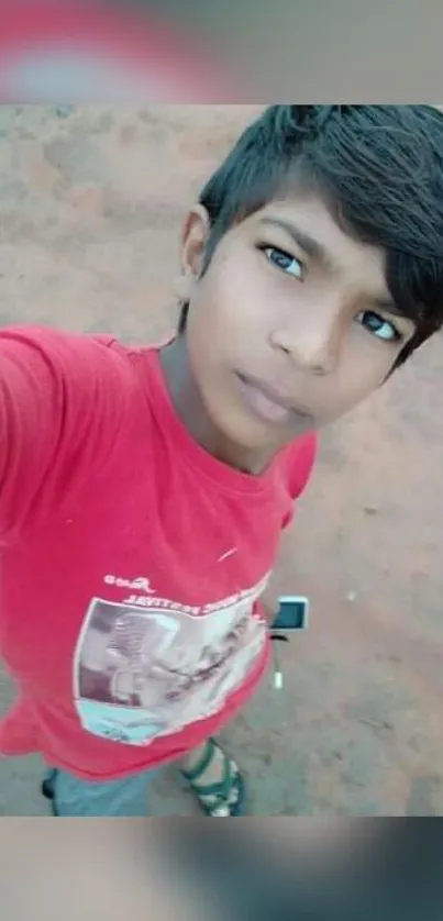 Young boy in red shirt posing outdoors.