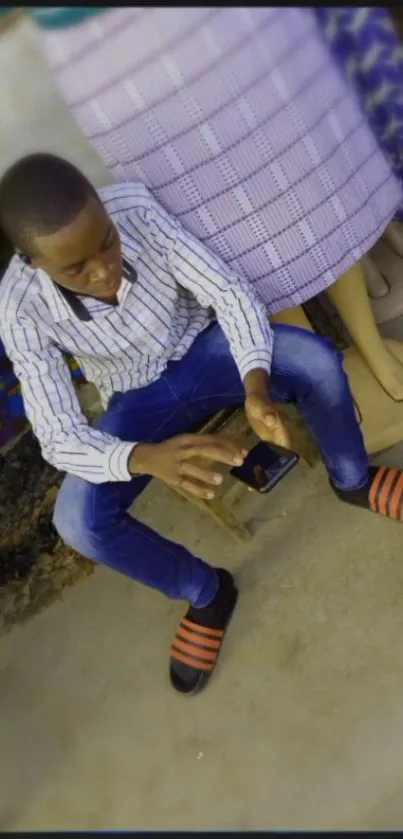 Young man in striped shirt sitting casually outdoors.