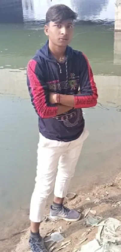 Young man in casual outfit stands by a calm riverbank, exuding a relaxed vibe.