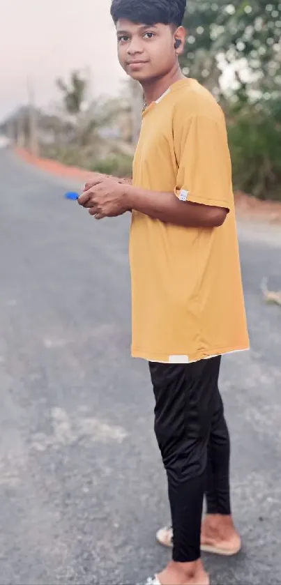 Young person in goldenrod shirt standing on quiet road.