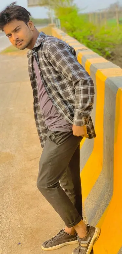 Young man in casual attire by a yellow roadside barrier.