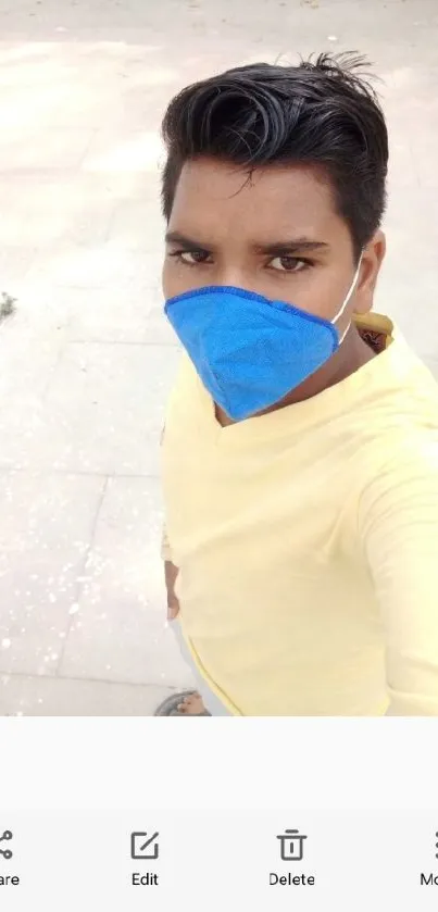 Person in yellow shirt and blue mask taking a selfie.