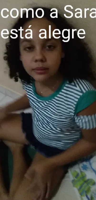 Young person in striped shirt sitting casually indoors.