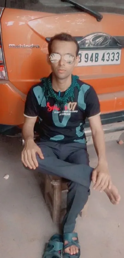 Man in casual outfit sitting by an orange car.