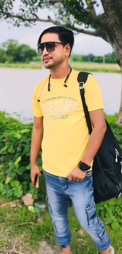 A person in a yellow shirt walking outdoors with a green backdrop.