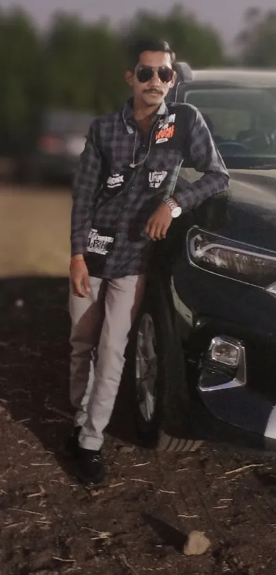 Man in casual outfit leaning on a black car.