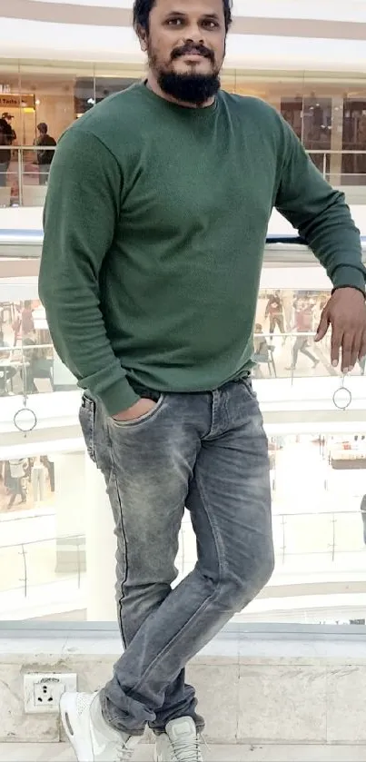 Man in a green sweater poses casually at shopping mall railing.