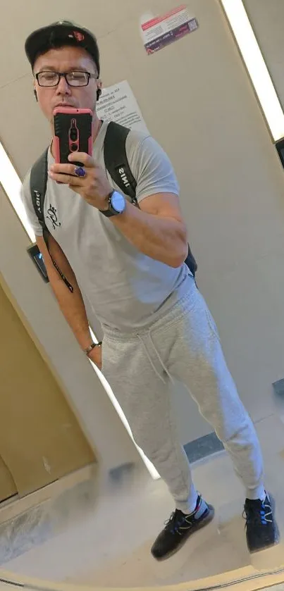 Man taking a mirror selfie in casual attire with neutral tones.