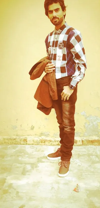 Man in casual checkered shirt and jeans against a yellow wall background.