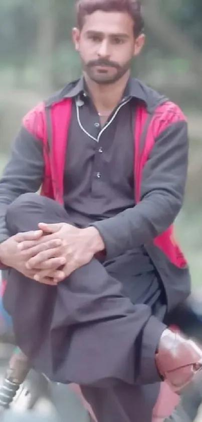 Man in red jacket seated outdoors, relaxed.