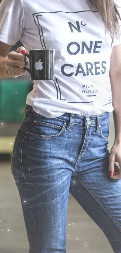 Person wearing casual jeans and a printed t-shirt holding a black mug.