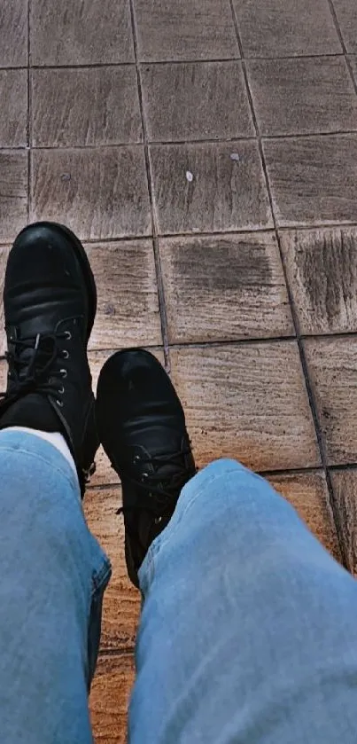 Casual view of black boots on textured brown tiles with blue jeans.