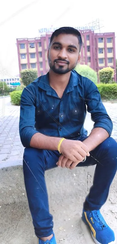 Man in navy shirt and jeans sitting outdoors.