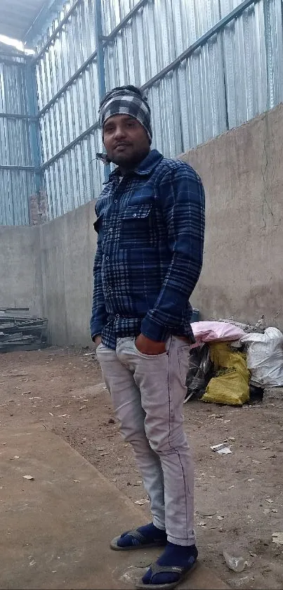 Man in plaid shirt standing in rustic warehouse.