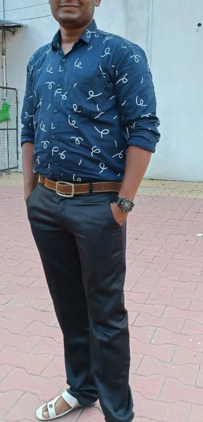 Man in blue shirt and black pants standing on a paved area.