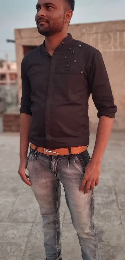 Stylish man in casual attire on a rooftop with a city backdrop.