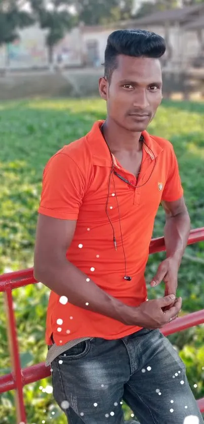 Man in bright orange shirt by lush green river.