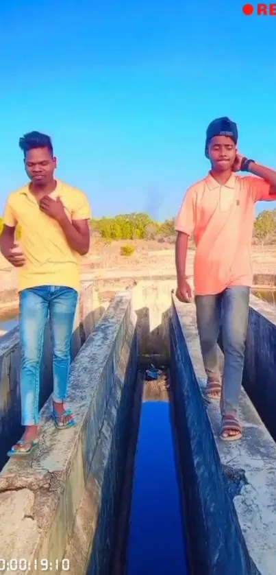 Two young men walking on a sunlit path under a bright blue sky.