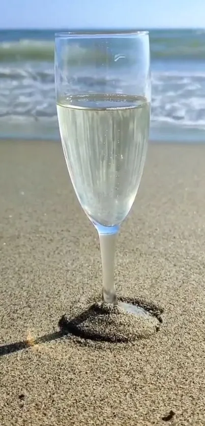 Champagne glass in beach sand by the ocean.