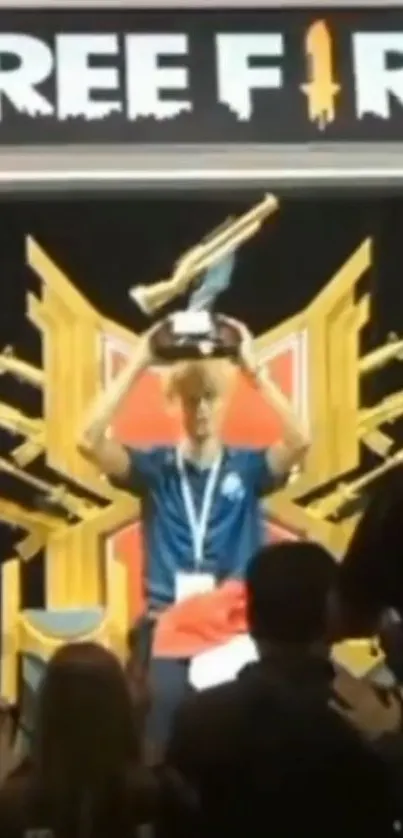 Gamer holds trophy on stage with Free Fire logo backdrop.