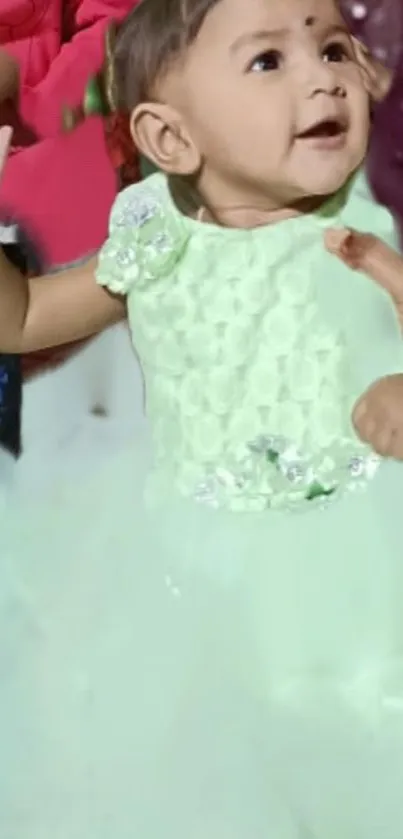 Baby in a pastel green dress, smiling adorably.