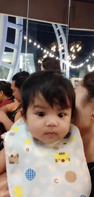 Cute baby in a warm, joyful setting with lights in the background.