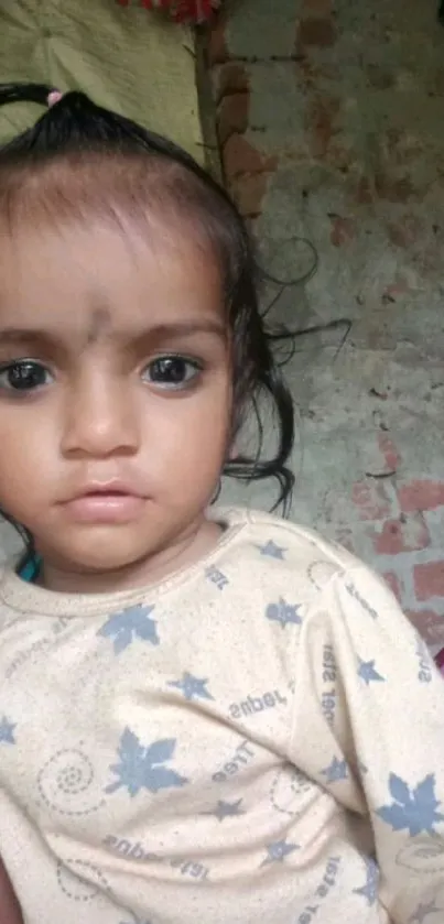 Cute baby with expressive eyes against rustic wall.