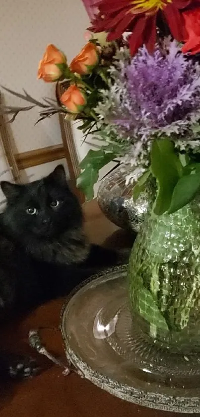 Black cat with floral vase displaying colorful blossoms on a table.